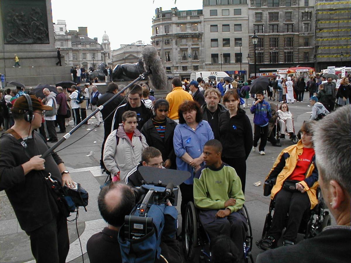 A photograph of a group of young disabled people including Mike at a demonstration in London. They are being filmed by a TV crew.
