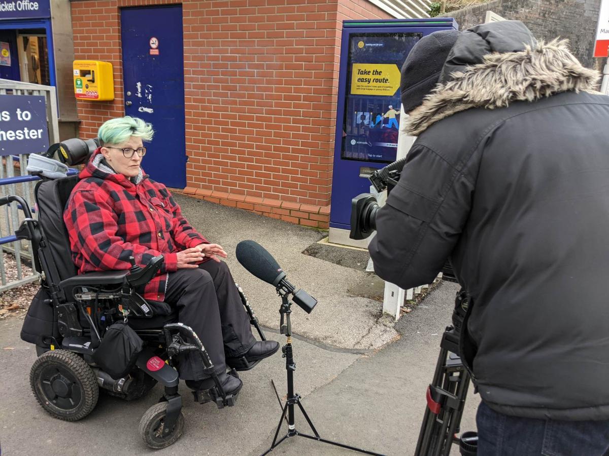 GMCDP board member Dennis, a power chair user, being interviewed for TV outside Mauldeth Road railway station in Manchester.