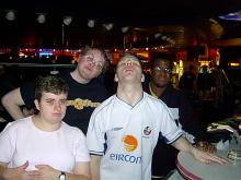 A photograph of a group of four young disabled people. Mike, a young white man with curly hair and glasses (back left)with friends from the young disabled people's forum. They are winding down in what looks like a bar with arcade machines in the background 