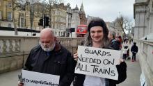 Two men walking along a street in London, possibly Whitehall, holding signs, One says "#DisabledByTheRailway", the other reads "guards needed on all trains". The man on the left is Kevin Greenan of NFBUK. On the right is GMCDP board member Pete.